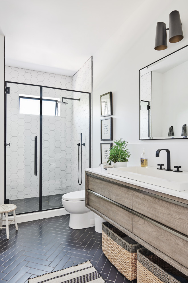 Photo of a mid-sized beach style 3/4 bathroom in Los Angeles with an alcove shower, a one-piece toilet, white tile, ceramic tile, white walls, ceramic floors, a drop-in sink, engineered quartz benchtops, black floor, a hinged shower door, white benchtops, flat-panel cabinets and light wood cabinets.