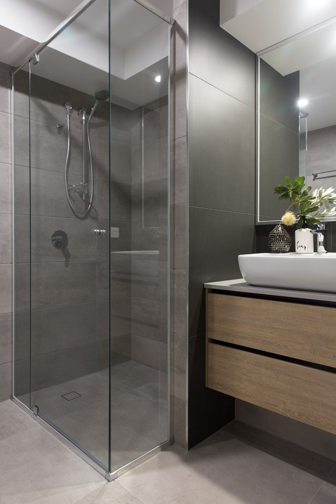 Design ideas for a small contemporary master bathroom in Sunshine Coast with flat-panel cabinets, light wood cabinets, a corner shower, a wall-mount toilet, gray tile, porcelain tile, grey walls, porcelain floors, a vessel sink, engineered quartz benchtops, grey floor, a hinged shower door and grey benchtops.