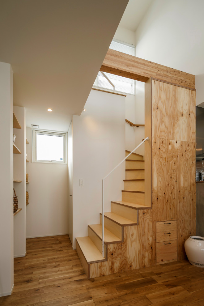 Стильный дизайн: изогнутая деревянная лестница среднего размера в стиле лофт с деревянными ступенями, металлическими перилами, обоями на стенах и кладовкой или шкафом под ней - последний тренд