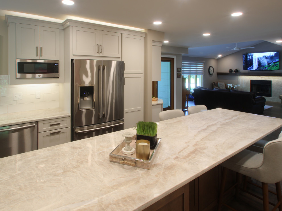 Eat-in kitchen - mid-sized transitional l-shaped brown floor eat-in kitchen idea with an undermount sink, shaker cabinets, white cabinets, quartzite countertops, white backsplash, ceramic backsplash, stainless steel appliances, an island and beige countertops