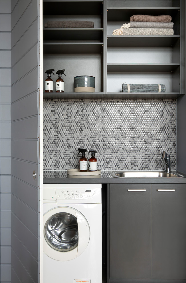 Inspiration for a small contemporary single-wall dedicated laundry room in Melbourne with a single-bowl sink, flat-panel cabinets, grey cabinets, quartz benchtops, grey walls, medium hardwood floors, a concealed washer and dryer, brown floor and grey benchtop.