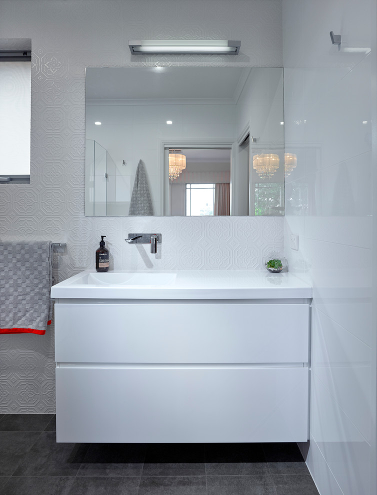 Photo of a small contemporary 3/4 bathroom in Other with white cabinets, an alcove shower, a one-piece toilet, white tile, porcelain tile, white walls, ceramic floors and an integrated sink.