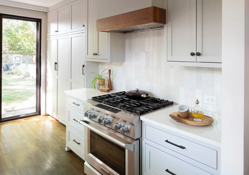 Inspiration for a small country eat-in kitchen in Raleigh with shaker cabinets, white cabinets, quartz benchtops, white splashback, ceramic splashback, stainless steel appliances, medium hardwood floors, a peninsula, brown floor and white benchtop.