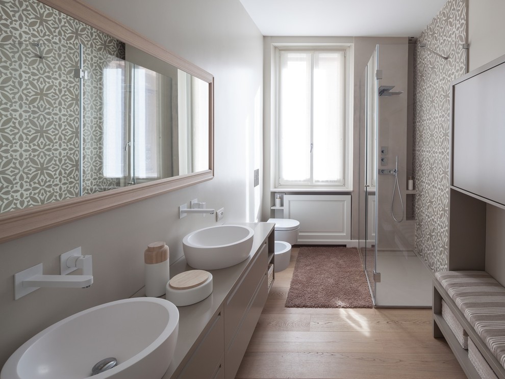 Inspiration for a large modern bathroom in Milan with flat-panel cabinets, beige cabinets, a curbless shower, a wall-mount toilet, beige tile, cement tile, beige walls, light hardwood floors, a vessel sink, solid surface benchtops, beige floor and a hinged shower door.