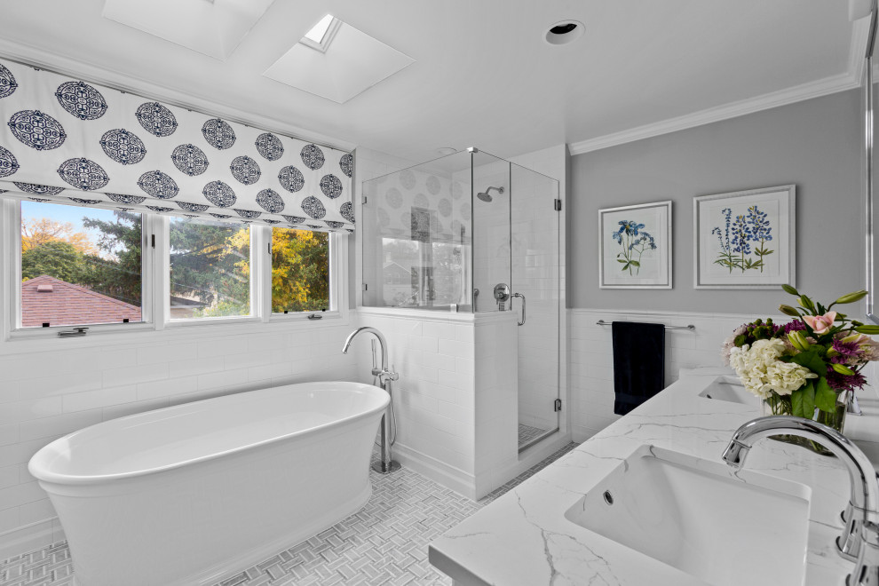 This is an example of a mid-sized transitional master bathroom in Chicago with shaker cabinets, white cabinets, a freestanding tub, a corner shower, a one-piece toilet, white tile, subway tile, grey walls, mosaic tile floors, a wall-mount sink, engineered quartz benchtops, grey floor, a hinged shower door, white benchtops, a niche, a double vanity and a freestanding vanity.