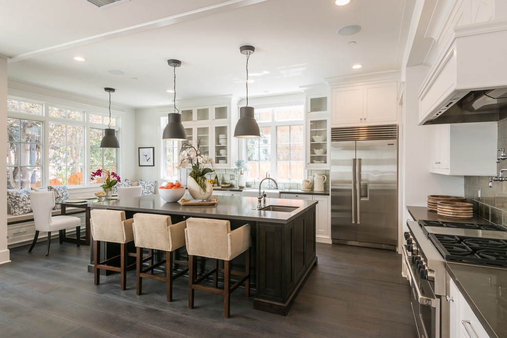 This is an example of a traditional l-shaped kitchen in Orange County with shaker cabinets, white cabinets, grey splashback, stainless steel appliances, medium hardwood floors, with island and brown floor.