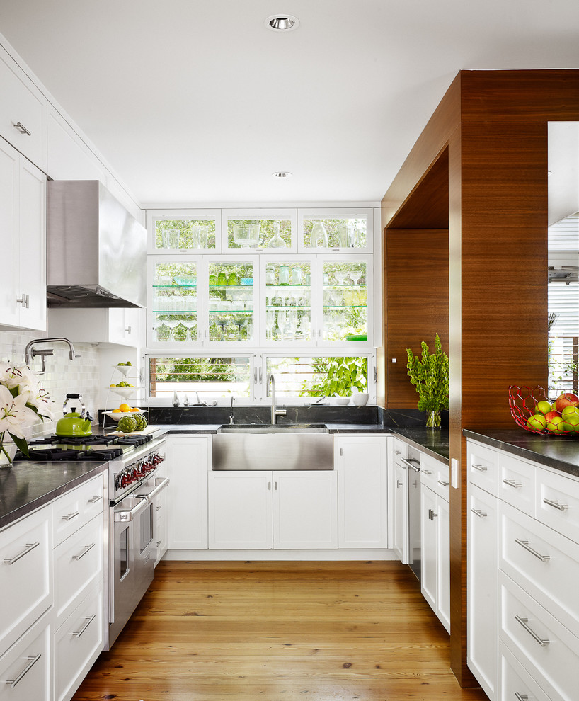 Inspiration for a midcentury kitchen in Austin with stainless steel appliances, a farmhouse sink, recessed-panel cabinets, white cabinets, white splashback and stone tile splashback.