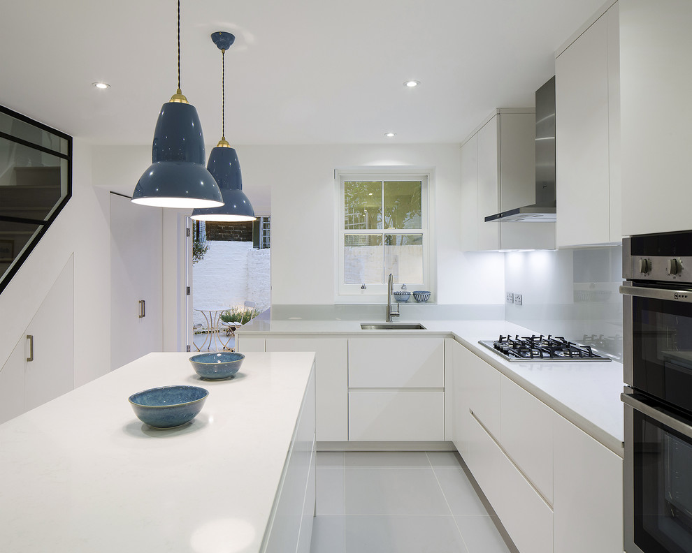 Photo of a large contemporary l-shaped eat-in kitchen in London with an undermount sink, flat-panel cabinets, white cabinets, quartzite benchtops, grey splashback, glass sheet splashback, stainless steel appliances, porcelain floors and with island.
