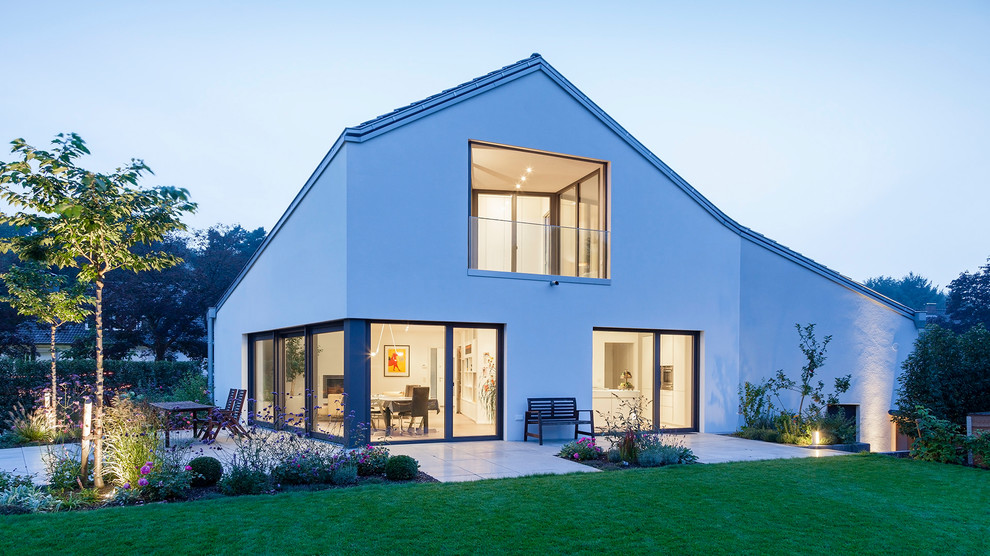 Photo of a mid-sized modern two-storey stucco white house exterior in Cologne with a gable roof and a shingle roof.