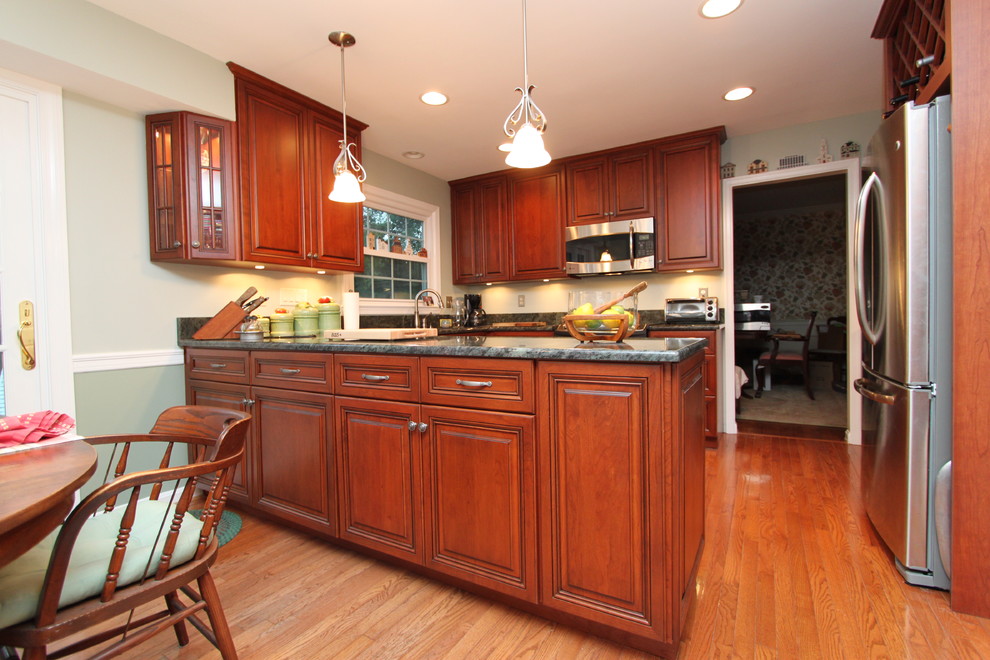 Photo of a traditional eat-in kitchen in Baltimore with raised-panel cabinets, medium wood cabinets, granite benchtops, green splashback, stainless steel appliances, medium hardwood floors and a peninsula.