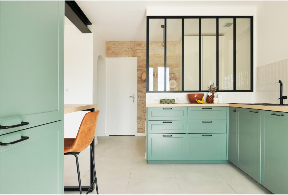 Photo of a large country l-shaped eat-in kitchen in Marseille with a double-bowl sink, beaded inset cabinets, green cabinets, wood benchtops, white splashback, subway tile splashback, panelled appliances, ceramic floors, a peninsula, grey floor, beige benchtop and exposed beam.