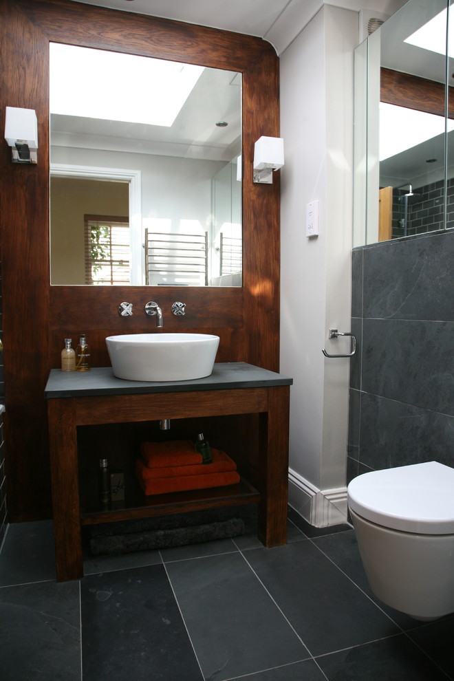 Photo of a mid-sized contemporary kids bathroom in Other with recessed-panel cabinets, dark wood cabinets, an alcove tub, a shower/bathtub combo, a wall-mount toilet, black tile, stone tile, white walls, slate floors, a vessel sink and granite benchtops.