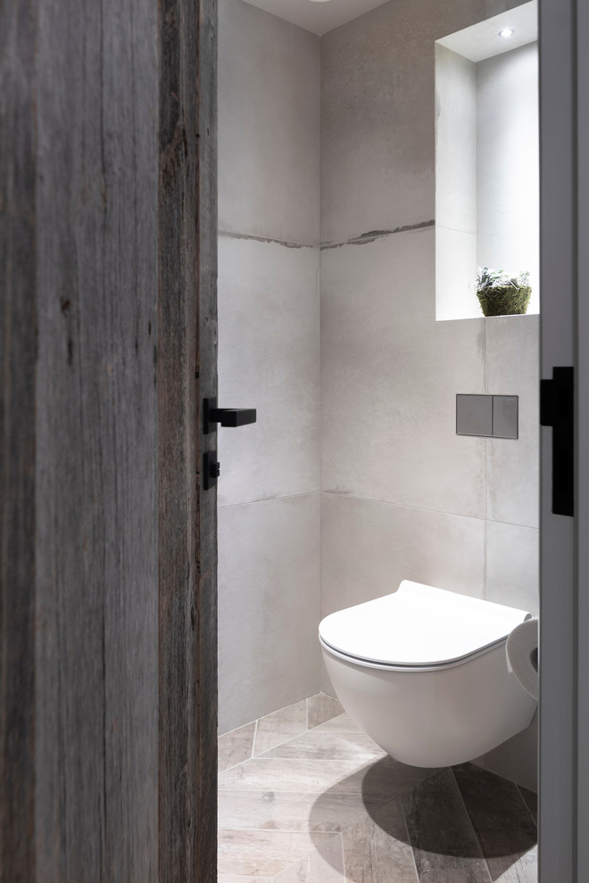 Design ideas for a mid-sized contemporary powder room in Cheshire with a wall-mount toilet, gray tile, porcelain tile, grey walls, porcelain floors, a trough sink, tile benchtops, grey floor and grey benchtops.