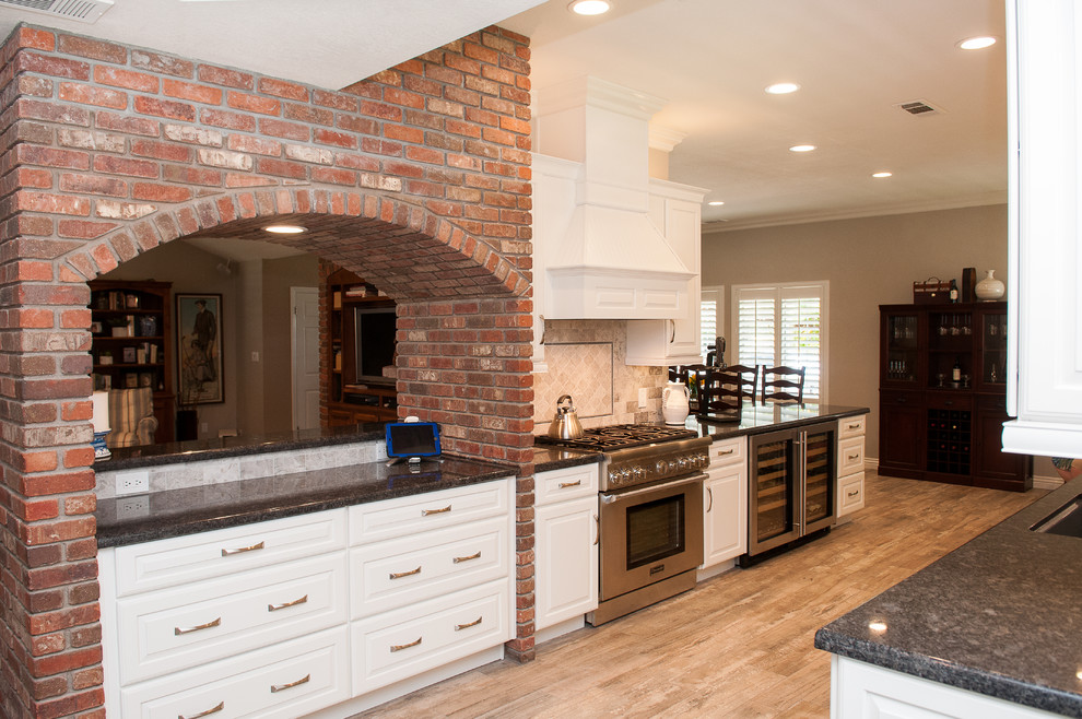 Mid-sized transitional galley porcelain tile and beige floor enclosed kitchen photo with a triple-bowl sink, raised-panel cabinets, white cabinets, granite countertops, beige backsplash, porcelain backsplash, stainless steel appliances and a peninsula