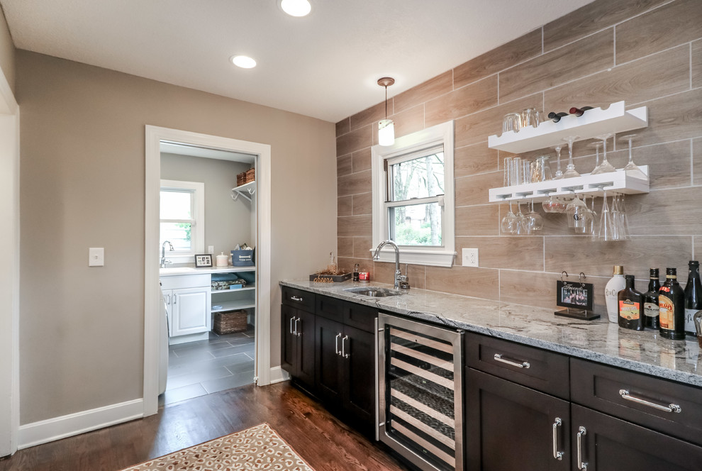 This is an example of a small transitional single-wall wet bar in Kansas City with an undermount sink, shaker cabinets, dark wood cabinets, granite benchtops, brown splashback, porcelain splashback, medium hardwood floors, brown floor and grey benchtop.