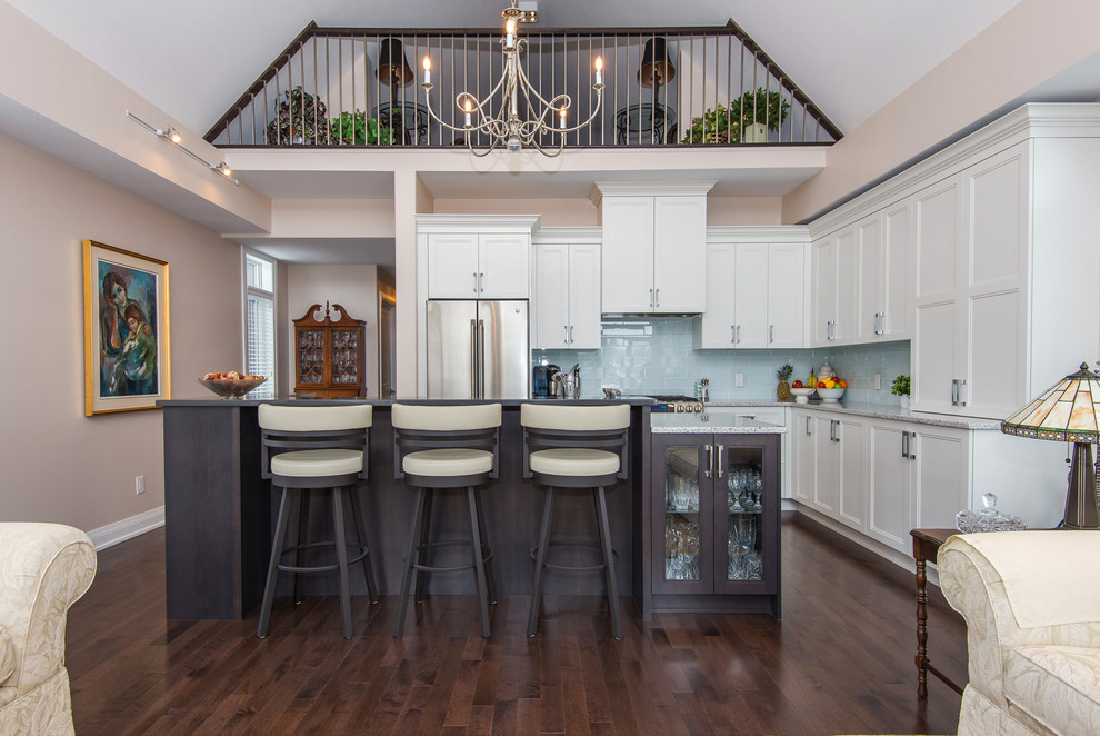 Inspiration for a mid-sized transitional l-shaped dark wood floor and brown floor open concept kitchen remodel in Ottawa with recessed-panel cabinets, white cabinets, quartz countertops, blue backsplash, subway tile backsplash, stainless steel appliances and an island