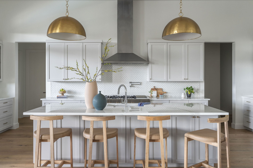 Transitional galley light wood floor and beige floor kitchen photo in Austin with white cabinets, white backsplash, mosaic tile backsplash, stainless steel appliances, an island, white countertops and shaker cabinets