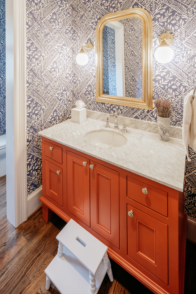 This is an example of an expansive arts and crafts powder room in Houston with red cabinets, blue walls, dark hardwood floors, an undermount sink, grey benchtops, shaker cabinets, engineered quartz benchtops, a freestanding vanity and wallpaper.