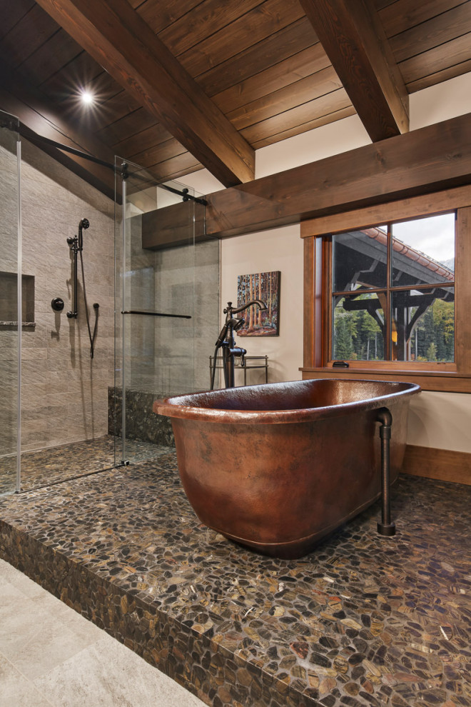 Large country master bathroom in Other with a freestanding tub, a curbless shower, beige tile, porcelain tile, pebble tile floors, a sliding shower screen, a shower seat, a niche, exposed beam, vaulted, wood, beige walls and brown floor.