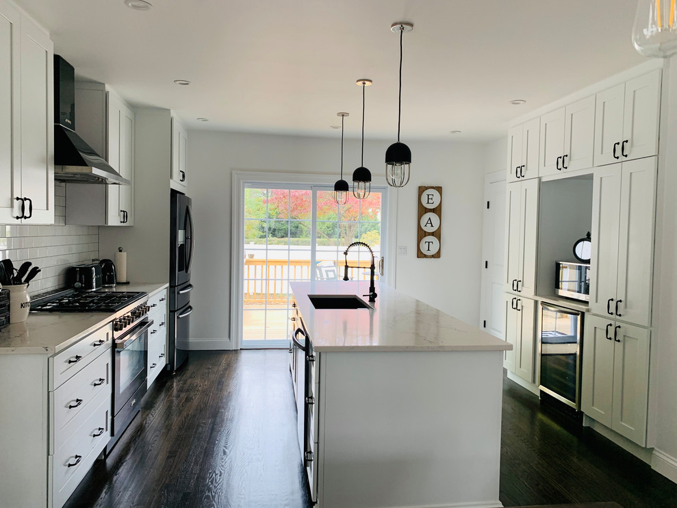 Mid-sized contemporary galley eat-in kitchen in New York with a drop-in sink, shaker cabinets, white cabinets, quartz benchtops, white splashback, porcelain splashback, black appliances, dark hardwood floors, with island, brown floor and beige benchtop.