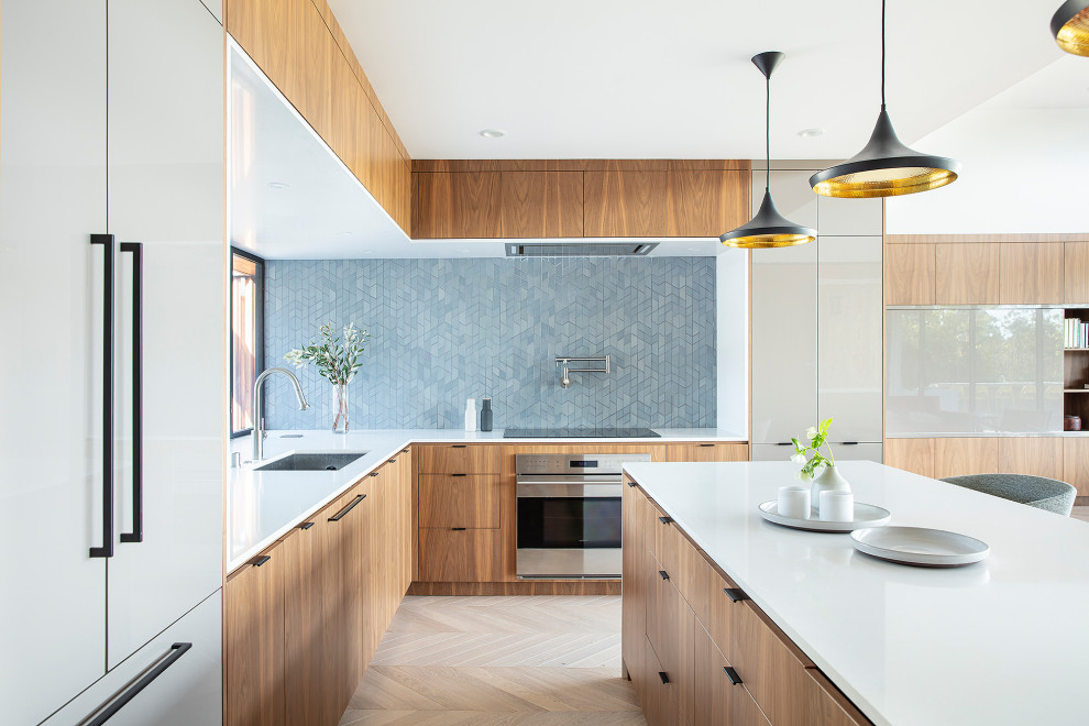 Cette photo montre une cuisine ouverte rétro en L et bois brun avec un évier 1 bac, un placard à porte plane, une crédence bleue, parquet clair, îlot et un plan de travail blanc.