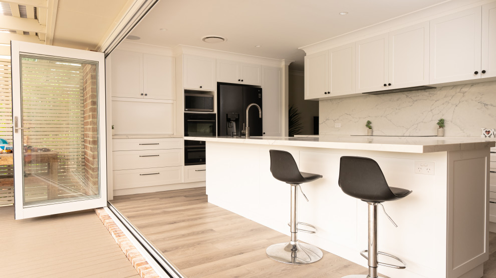 Exempel på ett stort klassiskt flerfärgad flerfärgat kök, med en undermonterad diskho, skåp i shakerstil, vita skåp, bänkskiva i kvarts, flerfärgad stänkskydd, rostfria vitvaror, mellanmörkt trägolv och brunt golv
