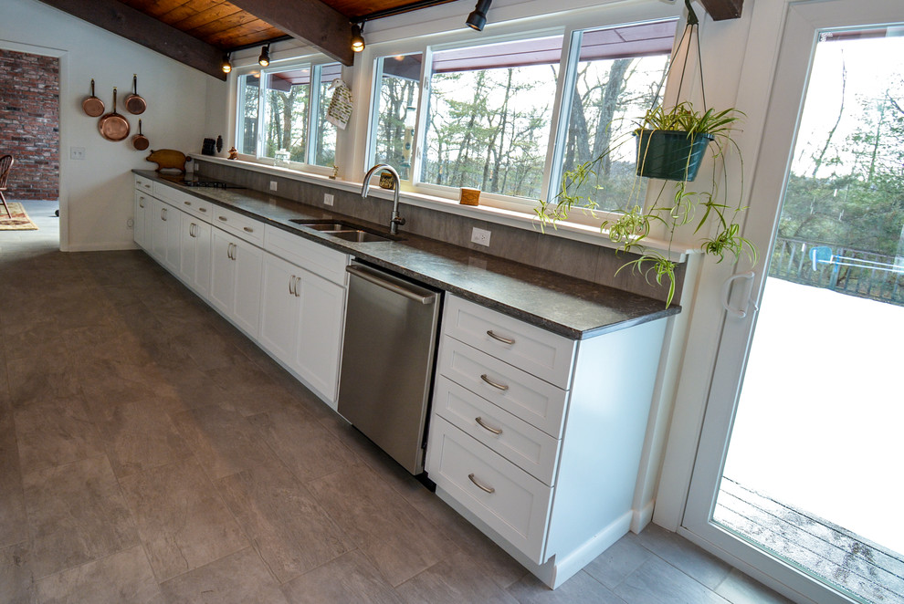 This is an example of a mid-sized midcentury galley separate kitchen in Boston with a double-bowl sink, flat-panel cabinets, white cabinets, quartz benchtops, stainless steel appliances, ceramic floors, grey benchtop, no island and brown floor.