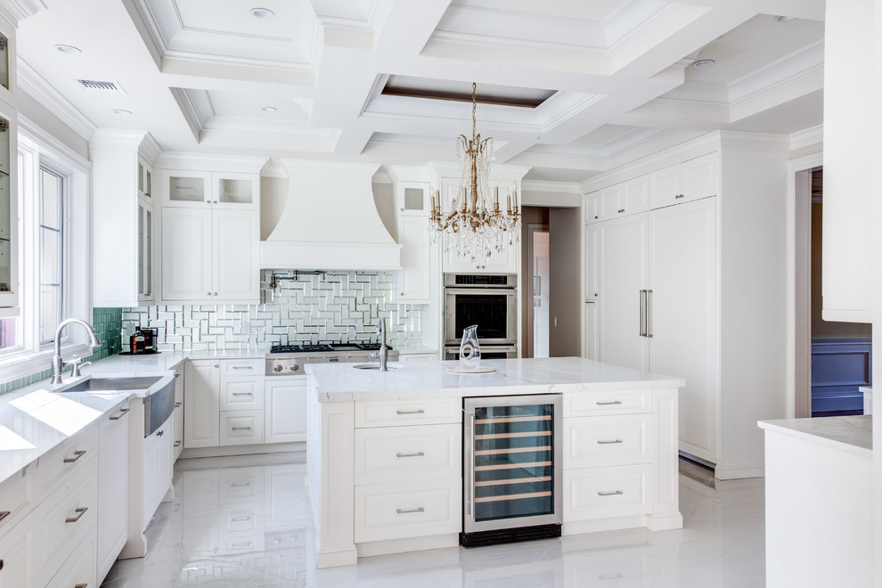 Photo of a mid-sized traditional u-shaped separate kitchen in New York with a farmhouse sink, raised-panel cabinets, white cabinets, blue splashback, glass tile splashback, with island, white floor and white benchtop.