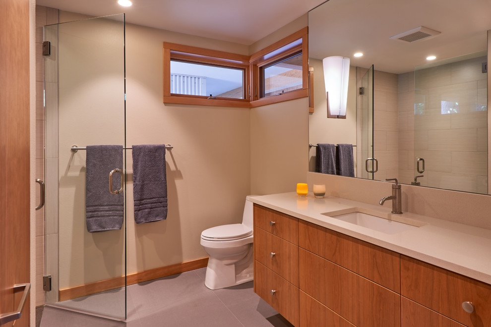 This is an example of a mid-sized contemporary 3/4 bathroom in Seattle with flat-panel cabinets, medium wood cabinets, an alcove shower, a one-piece toilet, white tile, porcelain tile, beige walls, porcelain floors, an undermount sink and solid surface benchtops.