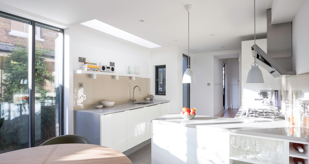 Mid-sized contemporary l-shaped eat-in kitchen in London with an integrated sink, glass-front cabinets, white cabinets, solid surface benchtops, beige splashback, stainless steel appliances, ceramic floors, beige floor and limestone splashback.