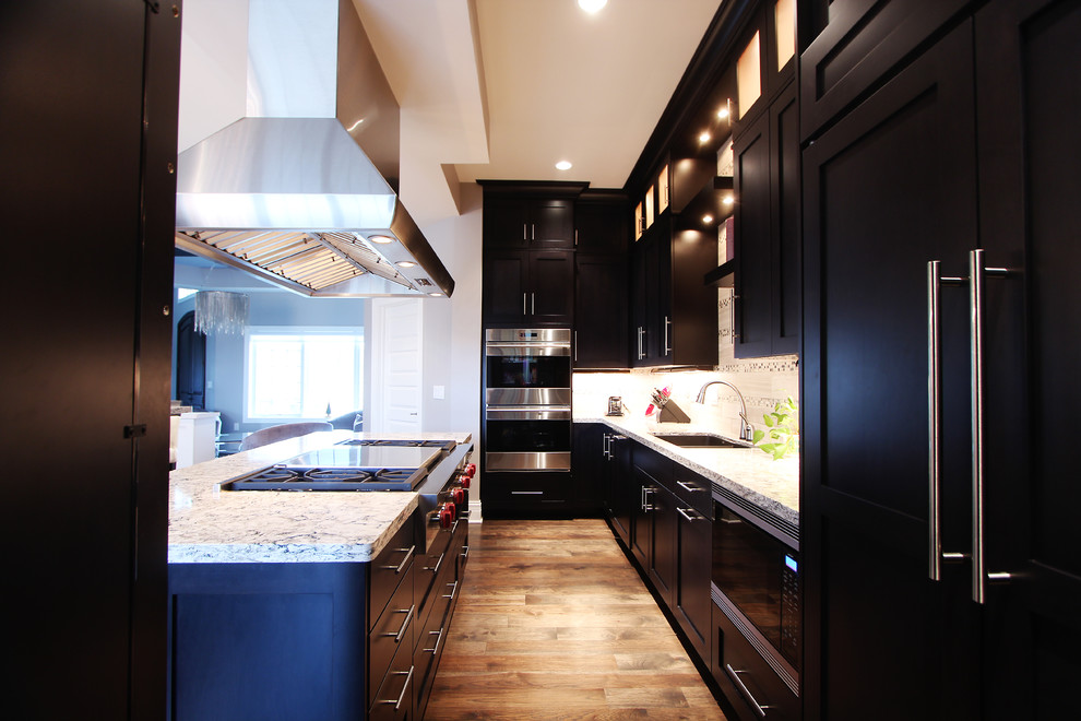 Large transitional u-shaped dark wood floor open concept kitchen photo with an undermount sink, recessed-panel cabinets, dark wood cabinets, quartz countertops, beige backsplash, stone tile backsplash, stainless steel appliances and two islands