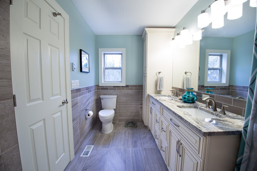 Photo of a mid-sized traditional 3/4 bathroom in New York with raised-panel cabinets, white cabinets, an alcove tub, a shower/bathtub combo, a two-piece toilet, brown tile, porcelain tile, blue walls, porcelain floors, an undermount sink, granite benchtops, brown floor, a shower curtain and grey benchtops.
