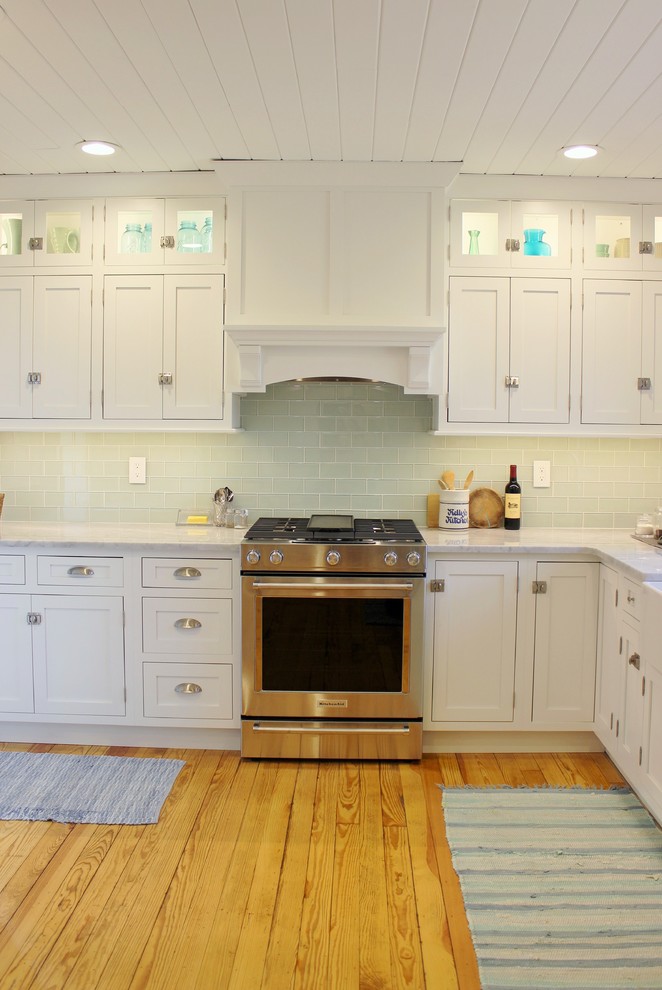 This is an example of a mid-sized country l-shaped eat-in kitchen in Other with a farmhouse sink, beaded inset cabinets, white cabinets, marble benchtops, green splashback, glass tile splashback, stainless steel appliances, light hardwood floors, no island, brown floor and white benchtop.