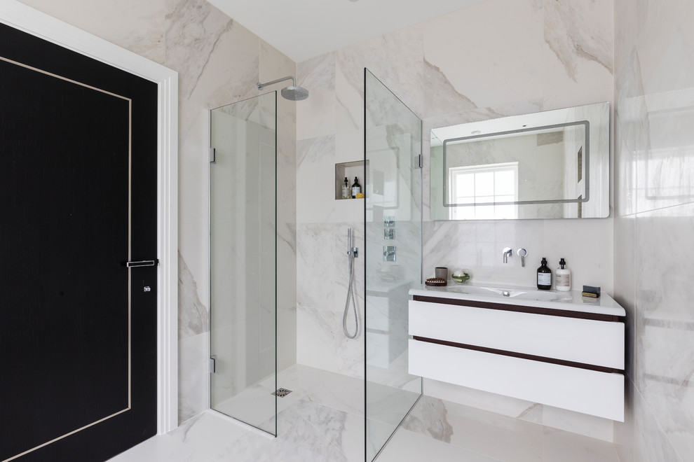 This is an example of a small contemporary 3/4 wet room bathroom in London with flat-panel cabinets, white cabinets, marble, marble floors, an open shower, a one-piece toilet, black and white tile, white tile, white walls, a wall-mount sink, solid surface benchtops, white floor and white benchtops.