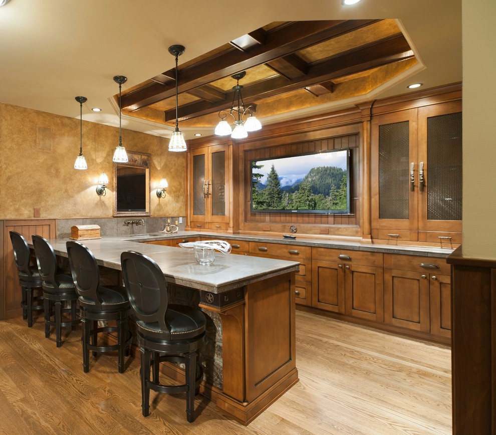 Inspiration for a large traditional u-shaped seated home bar in Other with shaker cabinets, medium wood cabinets, light hardwood floors, beige floor and grey benchtop.