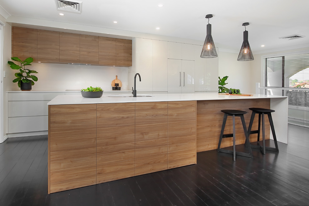 Photo of a mid-sized midcentury galley open plan kitchen in Sydney with an undermount sink, medium wood cabinets, quartz benchtops, white splashback, painted wood floors, with island, black floor and white benchtop.
