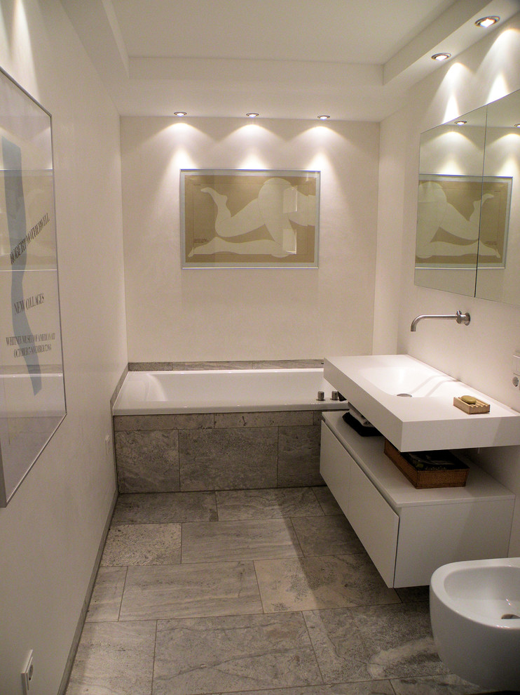This is an example of a small bathroom in Munich with a drop-in tub, gray tile, stone slab, white walls, a trough sink, solid surface benchtops and travertine floors.