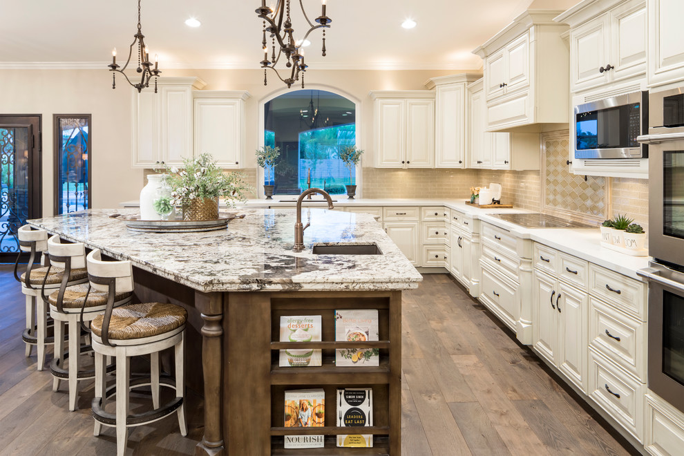 Inspiration for a large transitional l-shaped eat-in kitchen in Phoenix with an undermount sink, raised-panel cabinets, beige cabinets, beige splashback, glass tile splashback, stainless steel appliances, medium hardwood floors, with island, brown floor and quartz benchtops.