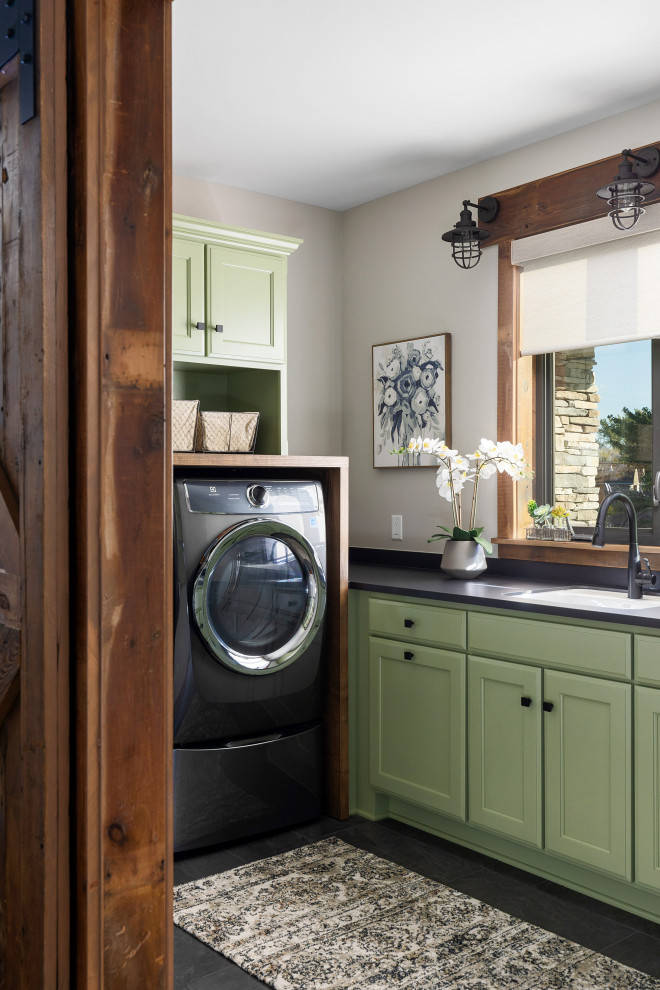 Exempel på en mellanstor lantlig svarta l-formad svart tvättstuga enbart för tvätt, med en nedsänkt diskho, luckor med infälld panel, gröna skåp, bänkskiva i betong, grå väggar, klinkergolv i keramik, en tvättmaskin och torktumlare bredvid varandra och svart golv
