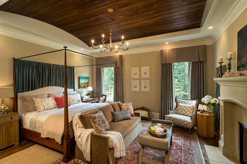 Photo of a large traditional master bedroom in Other with beige walls, a standard fireplace, dark hardwood floors, a stone fireplace surround and beige floor.