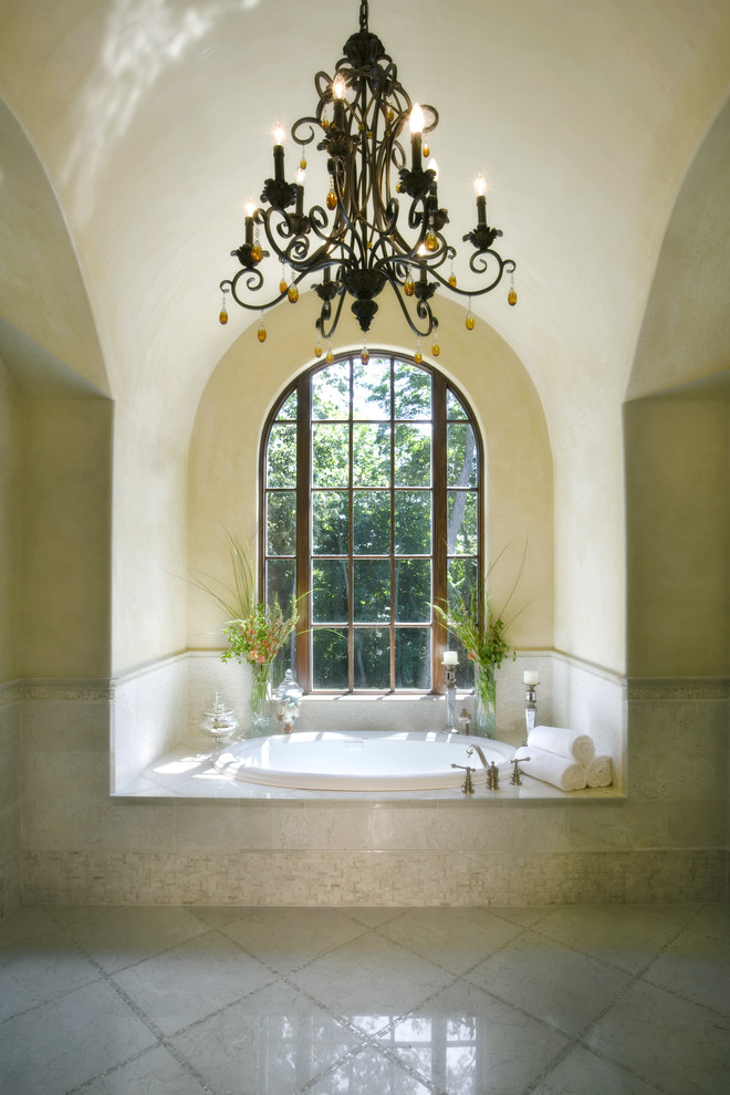 This is an example of a mediterranean bathroom in Austin with a drop-in tub, yellow walls, marble floors and beige floor.