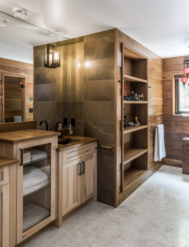 This is an example of a large country master bathroom in Other with shaker cabinets, light wood cabinets, a one-piece toilet, gray tile, marble, brown walls, porcelain floors, wood benchtops, grey floor, brown benchtops, a double vanity, a built-in vanity and panelled walls.