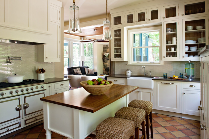 Photo of a mid-sized country l-shaped kitchen in New York with a farmhouse sink, recessed-panel cabinets, white cabinets, wood benchtops, glass tile splashback, coloured appliances, terra-cotta floors and with island.