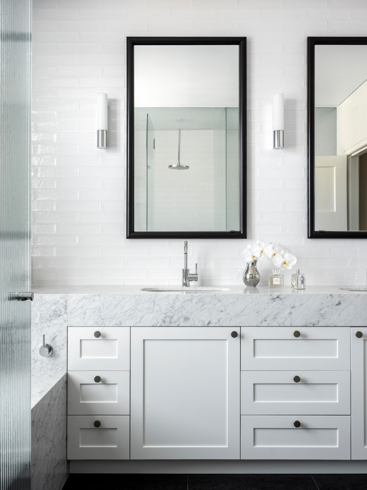 This is an example of a contemporary master bathroom in Sydney with white cabinets, an undermount tub, an alcove shower, a wall-mount toilet, white tile, ceramic tile, ceramic floors, marble benchtops, a hinged shower door, grey benchtops, an enclosed toilet, a double vanity, a built-in vanity and shaker cabinets.