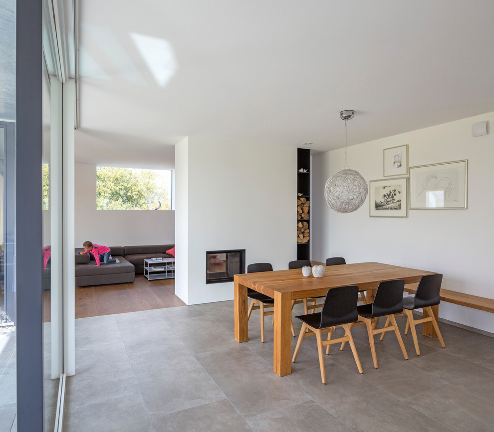 Large contemporary open plan dining in Other with white walls, concrete floors, a two-sided fireplace, a plaster fireplace surround and grey floor.