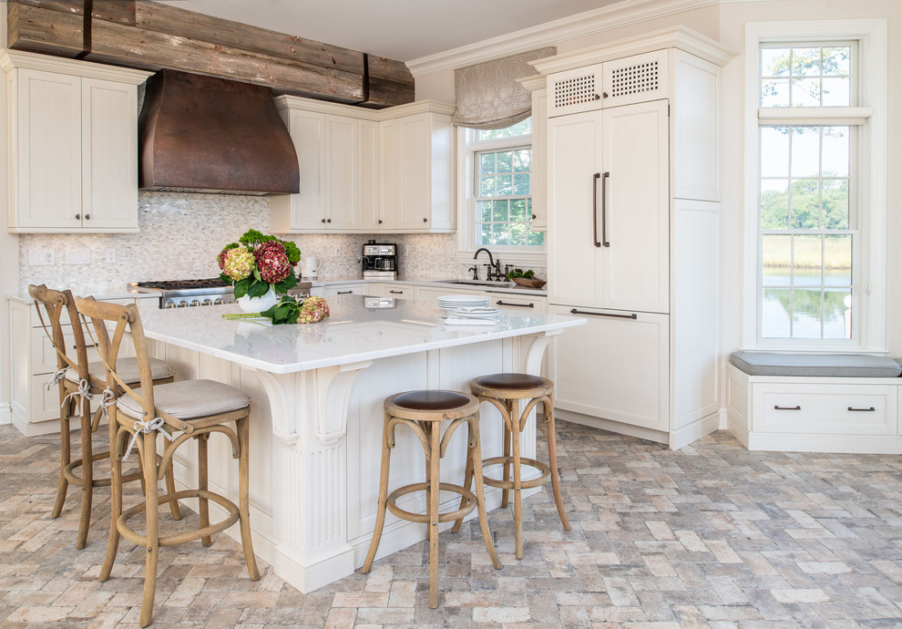 Beach style l-shaped kitchen in New York with an undermount sink, shaker cabinets, white cabinets, panelled appliances, with island, grey floor and white benchtop.