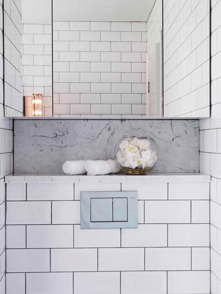 Inspiration for a mid-sized traditional kids bathroom in London with furniture-like cabinets, white cabinets, a drop-in tub, a shower/bathtub combo, a one-piece toilet, white tile, ceramic tile, white walls, mosaic tile floors, a pedestal sink, marble benchtops, white floor and a hinged shower door.