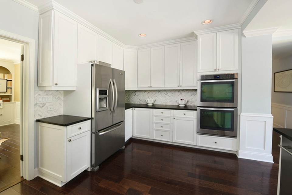 Example of a mid-sized transitional u-shaped dark wood floor and brown floor eat-in kitchen design in Chicago with an undermount sink, recessed-panel cabinets, white cabinets, quartz countertops, white backsplash, marble backsplash, stainless steel appliances, a peninsula and black countertops
