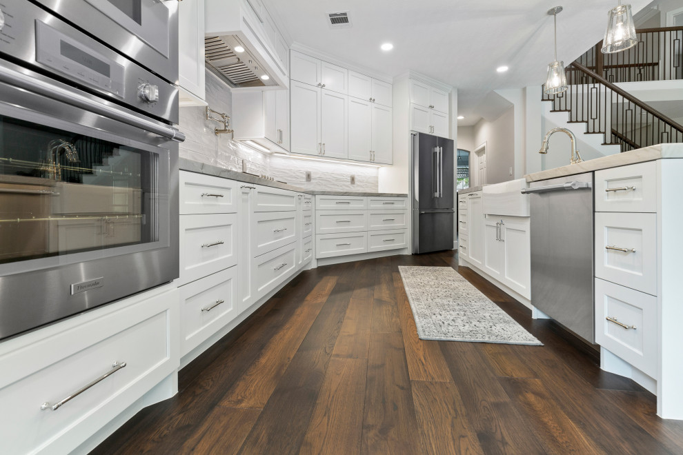 Inspiration for a mid-sized transitional single-wall dark wood floor and brown floor eat-in kitchen remodel in Houston with a farmhouse sink, beaded inset cabinets, white cabinets, quartzite countertops, gray backsplash, ceramic backsplash, stainless steel appliances, an island and gray countertops