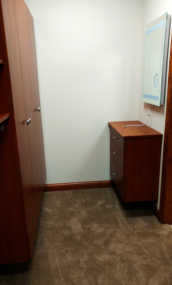 This is an example of an expansive midcentury gender-neutral walk-in wardrobe in Milwaukee with flat-panel cabinets, medium wood cabinets, carpet and grey floor.